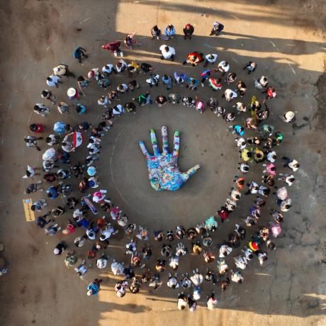 Photo is an aerial view of an embroidered hand surrounded by a crowd of young activists